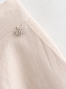 Detailed macro view of light beige linen trousers featuring a silver floral charm detail