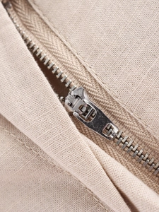 Detailed close-up of high-quality silver metal zipper on beige woven linen fabric