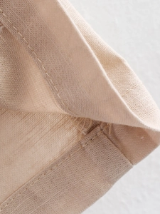 Detailed macro view of beige linen fabric texture and premium rolled hem stitching detail