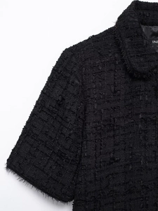 Close-up of black tweed dress fabric showing textured weave and frayed edge details