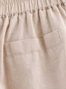 Detailed macro view of beige linen pants featuring elastic waistband and a sleek welt pocket