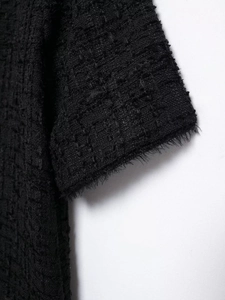 Detailed macro shot of black tweed dress sleeve with refined fringe edge and rich texture