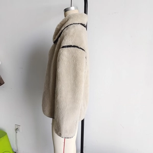 Detail view of beige faux fur jacket with dark contrast piping and cozy texture