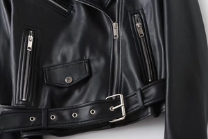 Detailed view of black faux leather biker jacket with silver zippers and belted waist