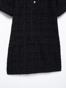 Close-up of black tweed fabric with a gold button and elegant frayed edges