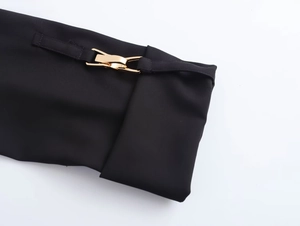 Dettaglio del polsino di un vestito nero con raffinata fibbia dorata e cinturino sottile
