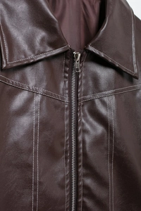 Détail de veste en similicuir marron foncé avec surpiqûres blanches et fermeture éclair