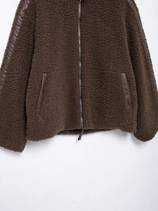 Detail of dark brown fleece jacket featuring faux leather piping and metal zipper closure