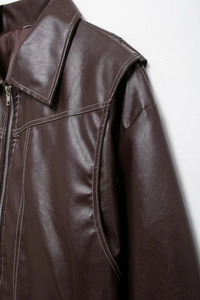 Détail de la veste en cuir PU marron foncé avec surpiqûres blanches et fermeture éclair métallique