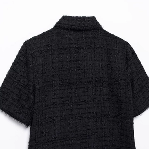 Back detail of a black tweed short sleeve jacket with fringed edges and textured fabric