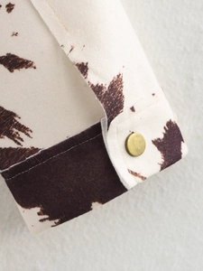 Détail d'une veste en laine imprimé vache avec un bouton en métal doré vintage chic