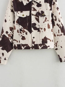 Détail d'une veste courte à imprimé vache avec motifs marrons et boutons en métal