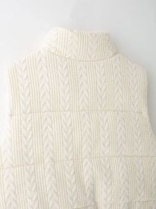 Makroansicht der cremefarbenen Strickweste mit Zopfmuster und hohem Stehkragen-Detail