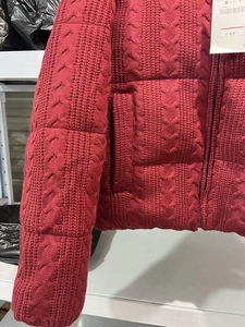 Detail der dunkelroten gesteppten Strickjacke mit Zopfmuster und Originaletiketten
