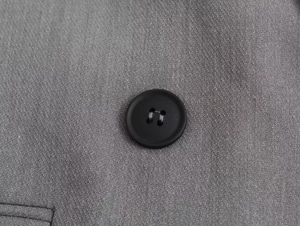 Makroaufnahme der grauen Twill-Stoffstruktur und des mattschwarzen Knopfs am Sakko