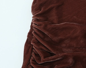 Détail des coutures froncées sur une robe en velours ocre foncé au fini brillant