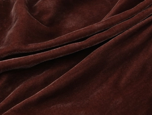 Détail du tissu en velours marron foncé montrant la texture douce et les plis élégants
