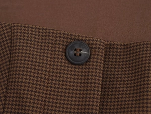 Macro shot of brown houndstooth fabric featuring a dark button and refined stitching detail