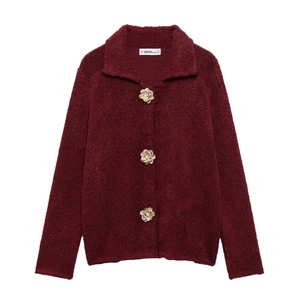 Dettaglio dei bottoni a fiore dorati su un cardigan in finta pelliccia rosso scuro