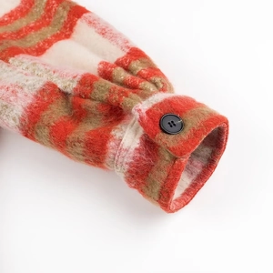 Close-up of orange and brown plaid wool sleeve cuff with a black button detail