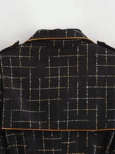 Close-up of black tweed fabric with gold threads and metallic buttons on long coat