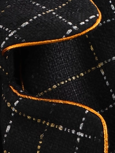 Detailed view of black tweed fabric with metallic gold thread and orange woven piping