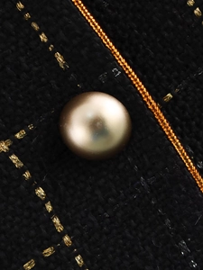 Macro shot of black and gold tweed fabric texture with a champagne pearl button detail