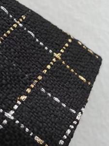 Macro shot of tweed fabric texture with black, gold, and silver metallic threads