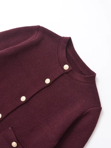 Close-up of burgundy knit cardigan featuring gold embossed buttons and pocket detail