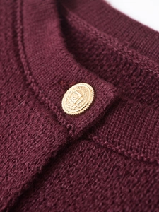 Macro shot of burgundy knit fabric texture featuring a vintage embossed gold button detail