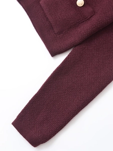 Detailed macro view of dark red knit texture and decorative gold button on the sleeve