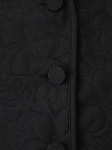 Detail of black quilted jacket featuring floral embroidery and matching fabric-covered buttons