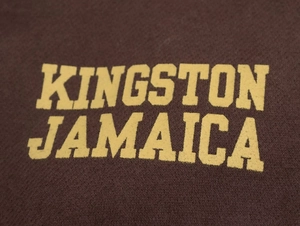 Dettaglio ravvicinato della stampa gialla Kingston Jamaica su tessuto felpa marrone scuro