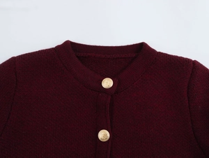 Close-up of burgundy knit cardigan neckline featuring ornate gold embossed buttons