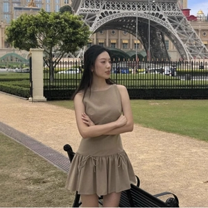 Elegant khaki sleeveless pleated dress with a decorative waist bow in an outdoor setting