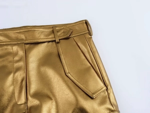 Détail du pantalon en similicuir doré métallisé avec plis à la taille et poche cargo