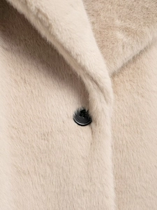 Detail of cream faux fur texture and a contrast black button on long winter coat
