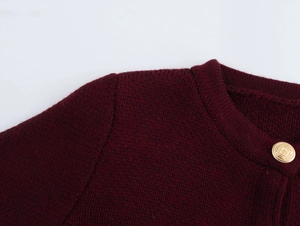 Close-up of burgundy knit cardigan featuring a decorative golden embossed button detail