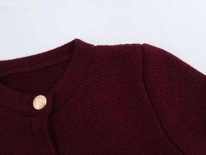 Close-up of wine red knit cardigan with round neck and gold embossed crest button