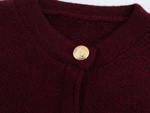 Detail of burgundy knit cardigan featuring a textured gold metal button on the crew neck