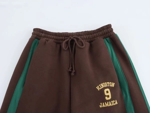 Dettaglio dei pantaloni sportivi marroni in cotone con strisce verdi e testo Kingston