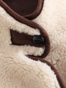 Detail of faux shearling texture with brown suede piping and a glossy black button on jacket