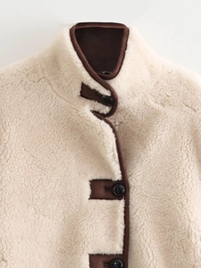 Detail of faux shearling jacket with brown leather trim and black round buttons