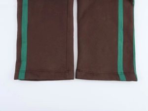 Dettaglio di pantaloni jogger marroni con strisce laterali verdi e cuciture doppie ai polsini