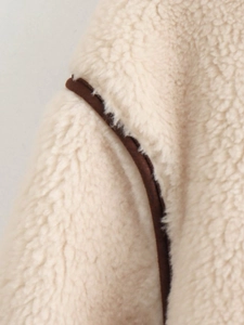 Detailed close-up of fluffy cream faux shearling jacket with dark brown stitched piping seams