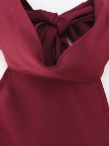 Detail of wine red halter dress showing sleek satin fabric and decorative back bow tie