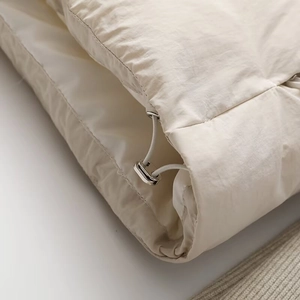 Detail of cream windproof fabric with elastic drawstring and silver metal toggle closure