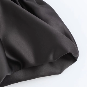 Detail showing the luxurious black satin fabric texture and silky smooth finish of the dress