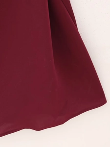 Detailed view of the dark red satin fabric hem with elegant draped folds on a white floor