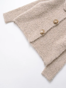 Détail d'un cardigan en maille bouclée beige avec boutons floraux dorés et perles élégantes
